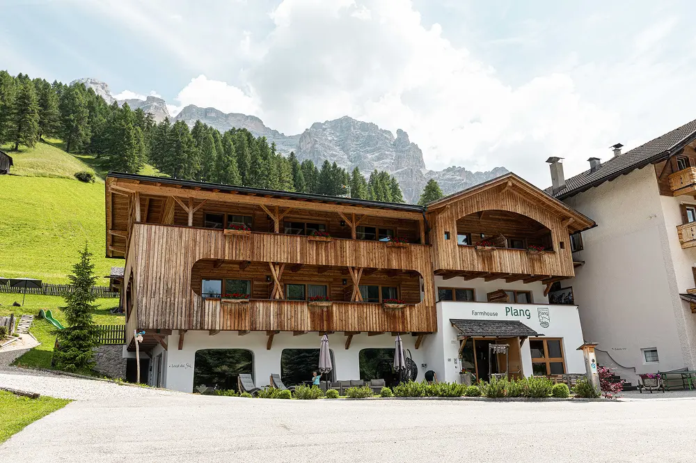 Die Außenansicht des Farmhouse Plang im Alta Badia zeigt die harmonische Kombination aus Holz und weißen Fassaden im alpinen Stil.
